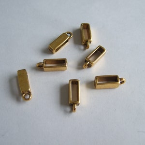 Peut inclure: Sept cadres de pendentif rectangulaires en métal doré avec des centres ouverts. Les cadres ont une boucle en haut pour être attachés à une chaîne ou un cordon.