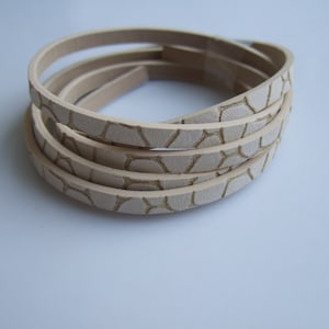 Könnte beinhalten: Ein Stapel aus vier beigefarbenen Lederriemen mit einem strukturierten Muster. Die Riemen sind aufgerollt und haben eine glatte, polierte Oberfläche.