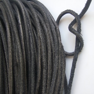 May include: A close-up of a spool of black leather cord. The cord is thick and has a rough texture.