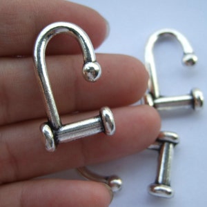Op de afbeelding: Verschillende zilverkleurige metalen U-vormige sluitingen. Elke sluiting heeft een afgeronde bovenkant en een cilindrische staaf aan de basis, met een kleine bal aan het einde van de U. Geschikt voor sieraden of knutselwerk.