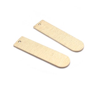 Puede incluir: Dos etiquetas rectangulares de metal de color dorado con bordes redondeados y un agujero en la parte superior. Las etiquetas tienen un acabado cepillado.