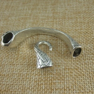 Könnte beinhalten: Silberfarbener Metall-Armbandverschluss mit einem dekorativen Haken und einem gebogenen, offenen Design.