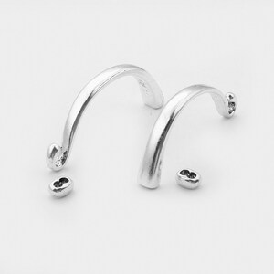 May include: Two silver metal hoops with a curved shape and a small silver metal connector.