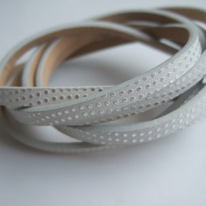 Puede incluir: Cordón de cuero blanco con un patrón de puntos. El cordón está enrollado y los puntos son visibles en la superficie.