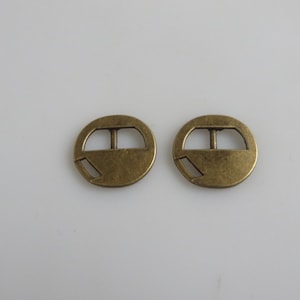 May include: Two antique gold-toned metal buckle closures. Each buckle is round with a rectangular opening in the center.