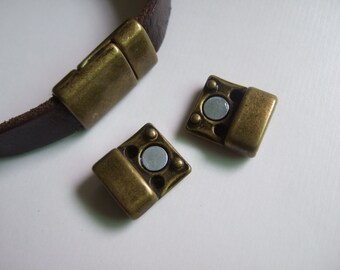 Könnte beinhalten: Zwei antike goldfarbene Magnetverschlüsse für Lederarmbänder. Die Verschlüsse sind quadratisch mit einem runden Magneten in der Mitte.