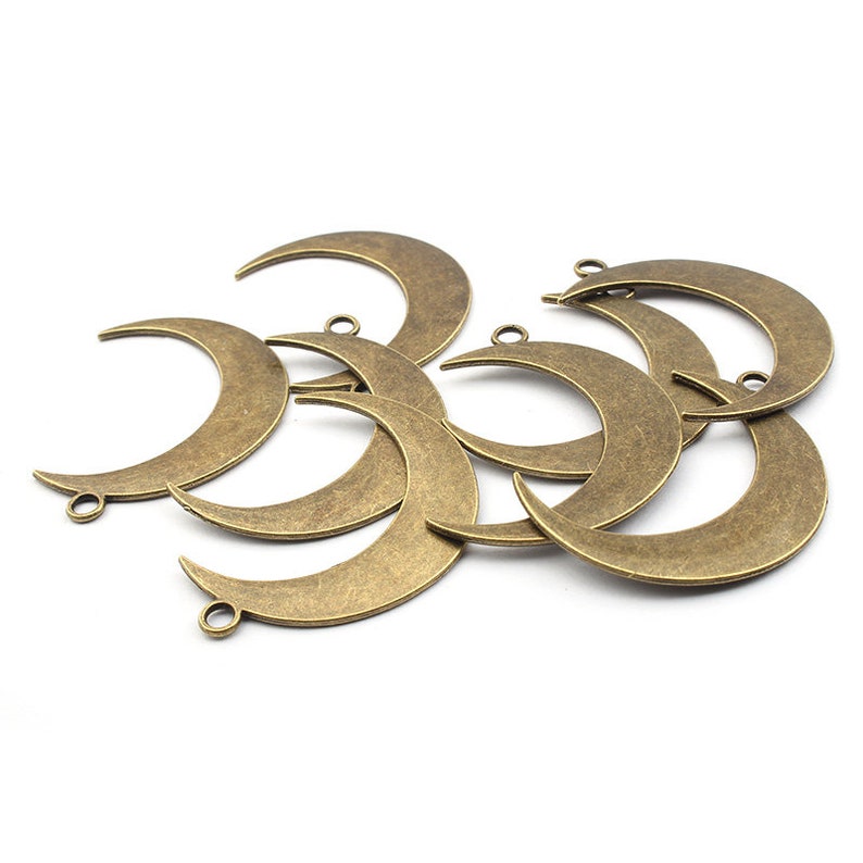 May include: A group of eight antique gold-toned metal crescent moon charms with a hole at the top for hanging.
