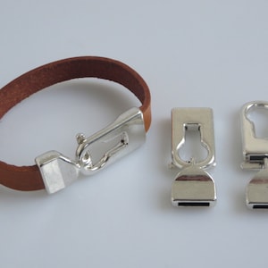 May include: A brown leather bracelet with a silver clasp and two silver clasps for attaching to a bag or other item.