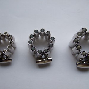 Puede incluir: Tres juegos de cierres magnéticos plateados para la elaboración de joyas. Cada juego incluye un par de cierres y una cadena de pequeñas cuentas plateadas.