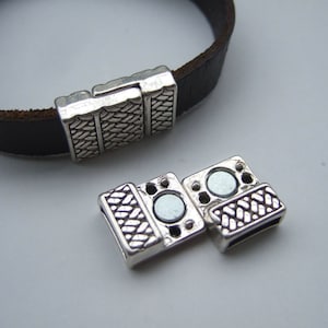 May include: Silver magnetic clasp for leather bracelets. The clasp has a woven design and is made of two pieces that connect with magnets.