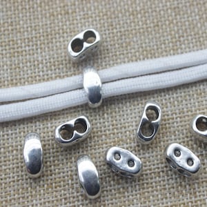 May include: Silver metal cord ends with a double loop design. The cord ends are shown on a white cord.