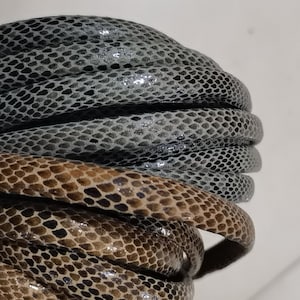 以下が含まれることがあります： 2つの革ひものロールのクローズアップ。上のロールは、ヘビの皮の模様のある濃いグレーです。下のロールは、ヘビの皮の模様のある薄い茶色です。