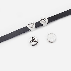 May include: Silver-toned metal beads with a Celtic knot design. The beads have a hole in the centre for threading onto a cord or leather strap. The beads are shown on a black leather strap.