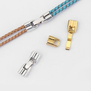 Puede incluir: Dos cierres metálicos plateados y dorados para cordones de cuero. Los cierres están diseñados para conectar dos piezas de cordón de cuero. Los cierres plateados se muestran unidos a un cordón de cuero marrón y azul.