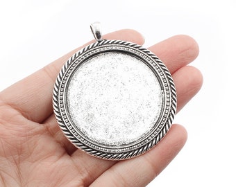 May include: Silver-toned round pendant with a decorative border. The pendant has a smooth, flat surface that is perfect for adding a custom design.