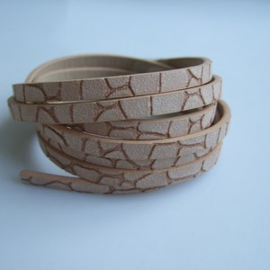 May include: A roll of beige leather cord with a textured, cracked pattern. The cord is approximately 1/2 inch wide.