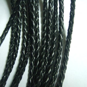 Può includere: Primo piano di un cordoncino in pelle intrecciata nero. Il cordoncino è realizzato con più fili di pelle intrecciati insieme per creare un cordoncino resistente e durevole.