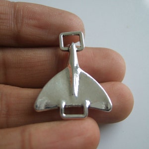 May include: Silver-toned metal charm shaped like a plane with a square loop at the top.