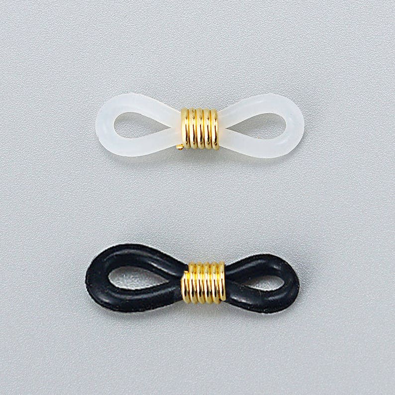 Pu&ograve; includere: Due paia di terminali per aste di occhiali, uno bianco e uno nero, con un connettore in metallo dorato al centro.