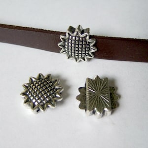 May include: Three silver metal charms for leather bracelets. Two charms are star-shaped with a textured centre and the third charm is a rectangle with a sunburst design.