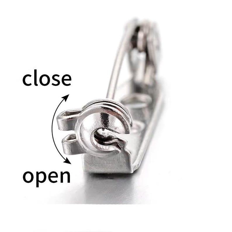 May include: Silver-toned safety pin with a spring-loaded clasp. The pin is open and the words "open" and "close" are written next to the pin.