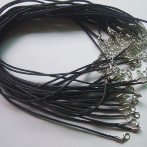 May include: A collection of black waxed cotton necklace cords with silver-colored clasps and extender chains. The cords are bundled together with a brown twine tie, ready for jewelry making or crafting projects.