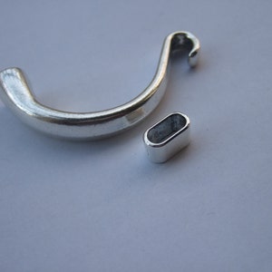 May include: Two silver metal jewelry findings. One is a curved hook with a loop at the end. The other is a small oval ring.