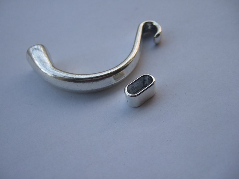 May include: Two silver metal jewelry findings. One is a curved hook with a loop at the end. The other is a small oval ring.