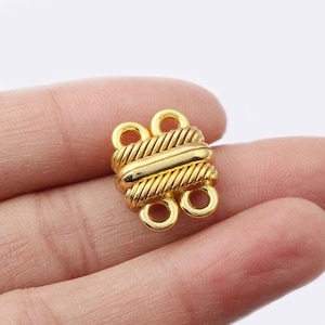 Puede incluir: Un cierre de joyería dorado con un diseño texturizado en forma de cuerda. El cierre tiene dos juegos de bucles para la fijación y una barra central. El metal tiene un acabado brillante y pulido.