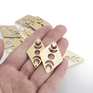 May include: A set of gold-toned metal charms featuring a crescent moon design. The charms are in the shape of a diamond and have a brushed finish.