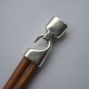 May include: Silver-toned metal clasp with a hook closure attached to a brown leather cord.