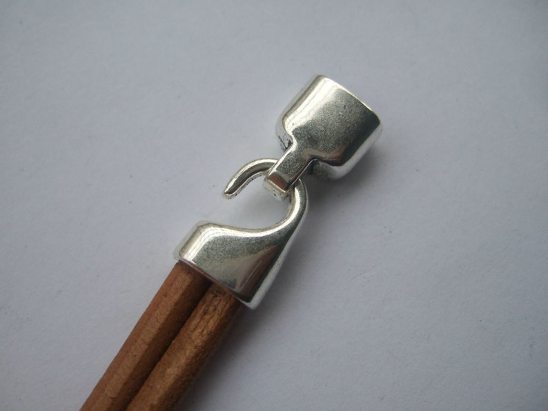 May include: Silver-toned metal clasp with a hook closure attached to a brown leather cord.