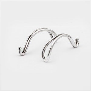 Könnte beinhalten: Ein silberner Metallständer mit zwei geschwungenen Armen. Der Ständer ist für die Präsentation kleiner Gegenstände wie Schmuck oder Figuren konzipiert.