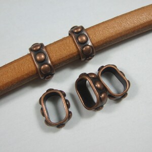 May include: Four copper-colored metal rings with a decorative pattern of small circles. The rings are designed to be used as a connector for leather straps or cords.