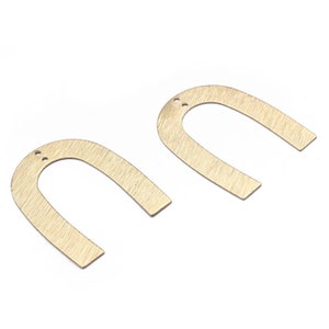 Puede incluir: Dos dijes de metal en forma de herradura de color dorado con acabado cepillado. Cada dije tiene dos pequeños agujeros en la parte superior.