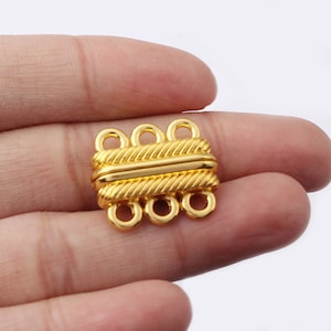 May include: Gold-toned metal clasp with four loops for attaching jewelry. The clasp has a textured design.
