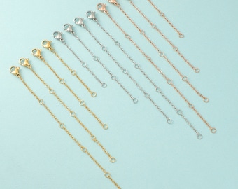 May include: A set of 10 gold, silver, and rose gold extender chains for necklaces or bracelets. The chains are all the same length and have a lobster clasp on one end and a jump ring on the other.