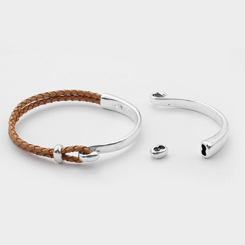 May include: A brown leather bracelet with a silver metal clasp. The bracelet is made of two strands of leather that are braided together. The clasp is a simple, curved design.