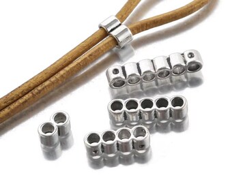 May include: Silver-toned metal slider beads with multiple circular holes for cord threading. The set includes a two-hole bead, a four-hole bead, a five-hole bead, and a six-hole bead, shown alongside a tan leather cord with a single slider bead.