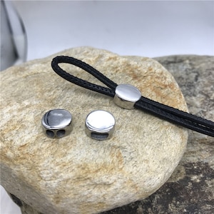 Könnte beinhalten: Drei silberne Metall-Kordelstopper. Zwei der Stopper haben ein Loch auf jeder Seite. Der dritte Stopper hat ein einzelnes Loch.