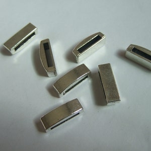 Puede incluir: Ocho piezas de conexión de metal plateado para la elaboración de joyas. Las piezas son rectangulares con una pequeña abertura en el centro.