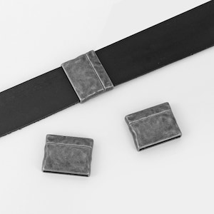 Könnte beinhalten: Drei silberfarbene Metallschließen für Lederriemen. Die Schließen haben eine strukturierte, gealterte Oberfläche.