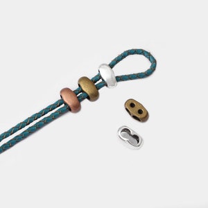 Könnte beinhalten: Ein geflochtenes Lederband in Türkis mit silbernen und bronzenen Metallperlen und zwei silbernen Metallverschlüssen.