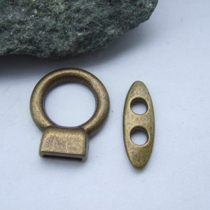 Puede incluir: Dos piezas de herrajes de metal dorado antiguo para un bolso o cartera. Una es un anillo redondo con una base cuadrada y la otra es un óvalo largo con dos agujeros.