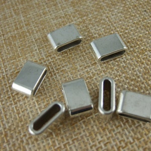 May include: Silver metal connector charms with a rectangular shape and a small opening in the centre. The charms are arranged on a woven fabric background.