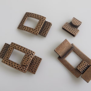 May include: Four antique gold-toned metal clasps with a textured surface. The clasps are in various shapes and sizes, with some featuring a square opening.