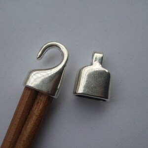 May include: Two silver metal cord ends, one with a hook and the other with a loop. The cord ends are designed to be used with a cord or rope.