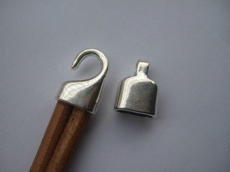 May include: Two silver metal cord ends, one with a hook and the other with a loop. The cord ends are designed to be used with a cord or rope.