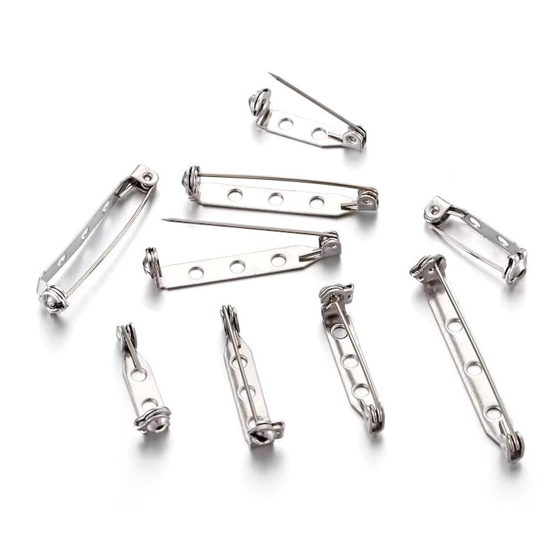 May include: A set of ten silver-toned metal safety pin backs. The pins are all the same size and shape, and they have a simple, classic design.