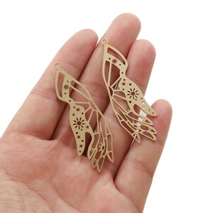 Peut inclure: Deux breloques en métal doré en forme de mains avec des motifs découpés complexes. Les mains sont ornées de petites étoiles et d'un motif en forme de soleil plus grand.
